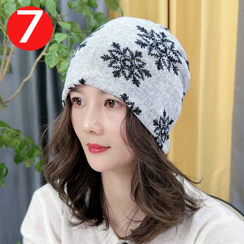 Woman wearing a gray beanie with black floral patterns, sitting outdoors with plants and a yellow curtain in the background.