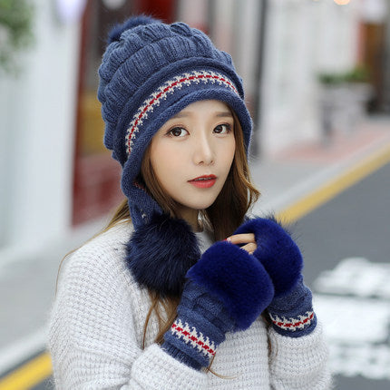 Woman wearing a blue knitted hat, scarf, and gloves with a blurred street background