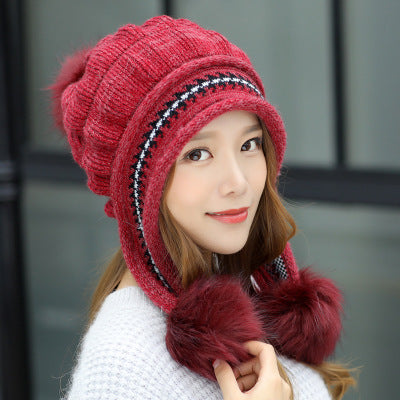 Woman wearing a red knitted hat with pom-poms against a blurred background