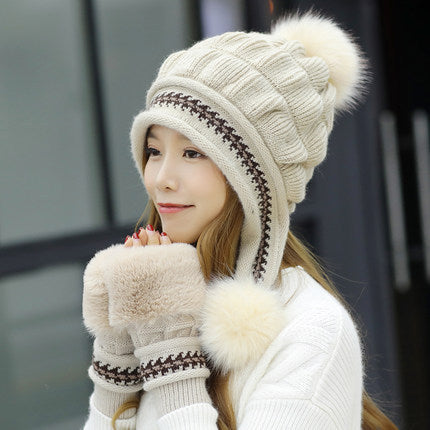 Woman wearing a cream-colored knitted hat with pom-poms and matching scarf.