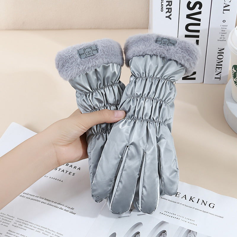 Gray gloves with fur cuffs held by a hand on top of books.