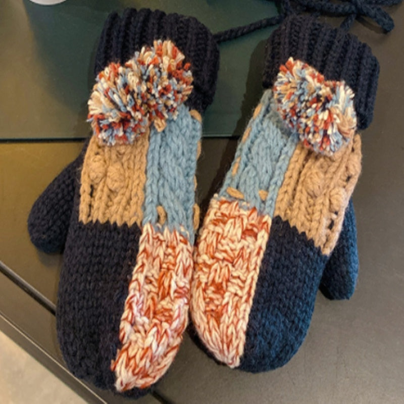 Pair of knitted mittens with pom-poms on a reflective surface