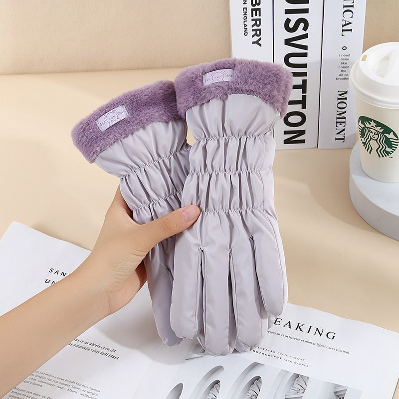 Gray gloves with purple cuffs held by a hand on top of a magazine with a Starbucks cup in the background.