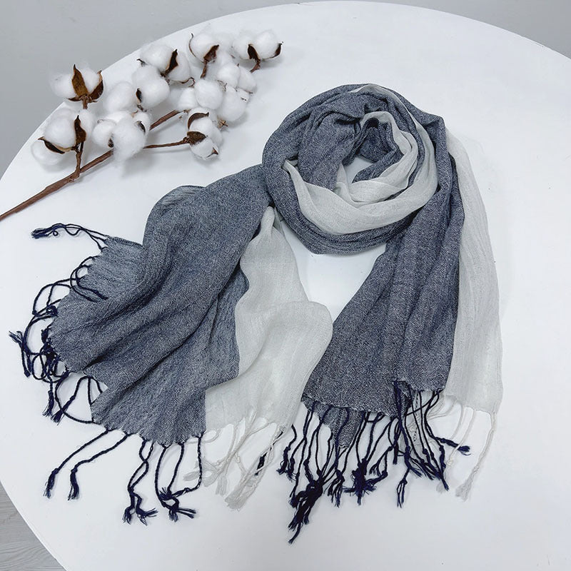 Gray scarf with tassels on a white surface with cotton branches.
