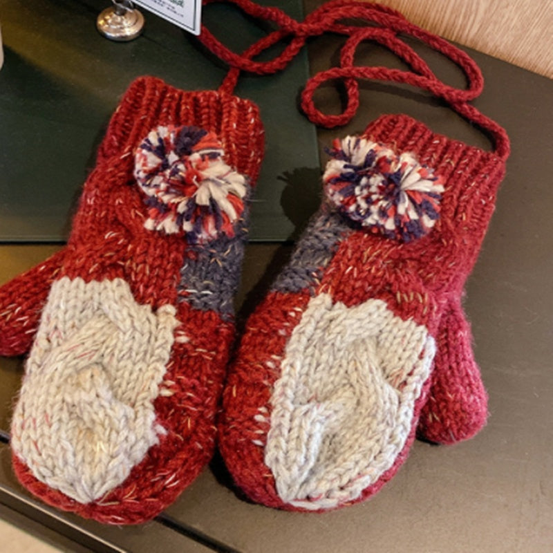 Pair of red knitted mittens with pom-pom accents on a wooden surface.