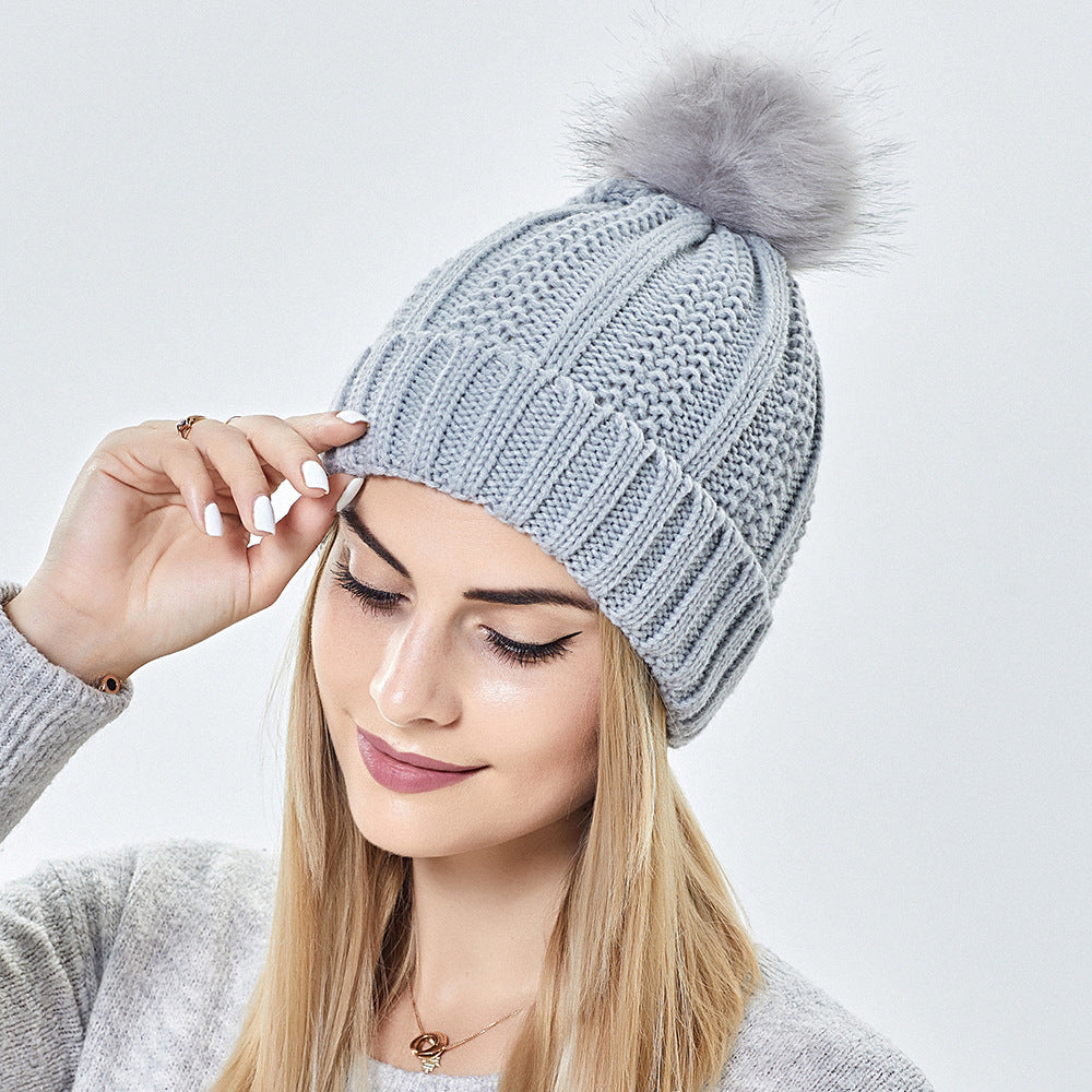 Woman wearing a gray knit beanie with a pom-pom on a light gray background
