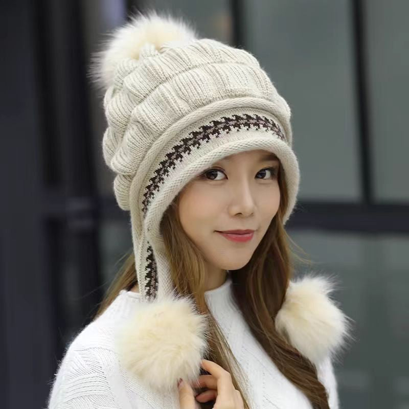 Woman wearing a beige knitted hat with pom-poms and a white scarf against a blurred background