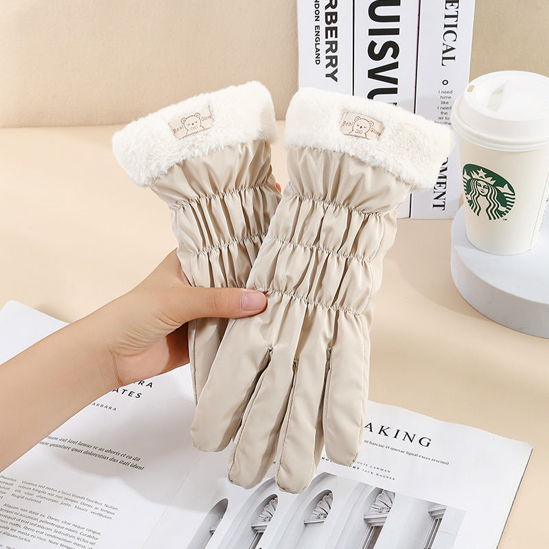 Beige gloves with white fur trim held by a hand on a surface with a magazine and Starbucks cup in the background.