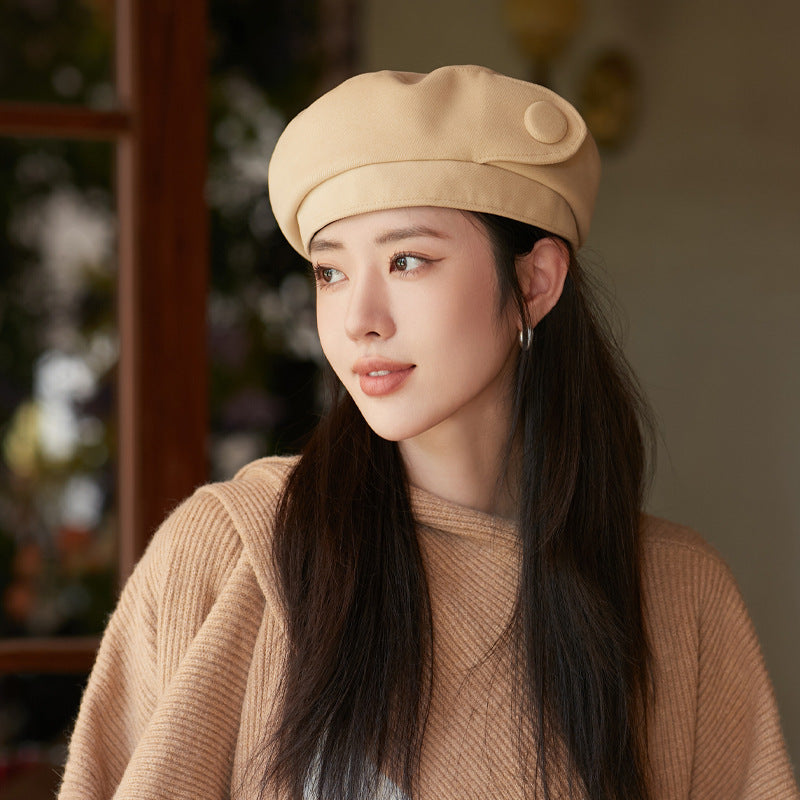 Woman wearing a beige beret and sweater in a blurred indoor setting