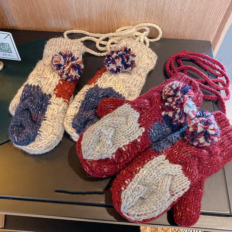 Pair of knitted baby booties with colorful pom-poms on a dark surface.