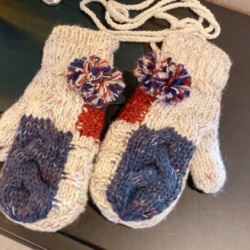 Pair of knitted mittens with colorful pom-poms on a dark surface