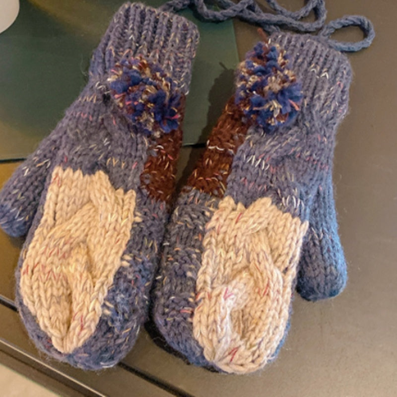 Pair of blue knitted mittens with beige cuffs on a reflective surface